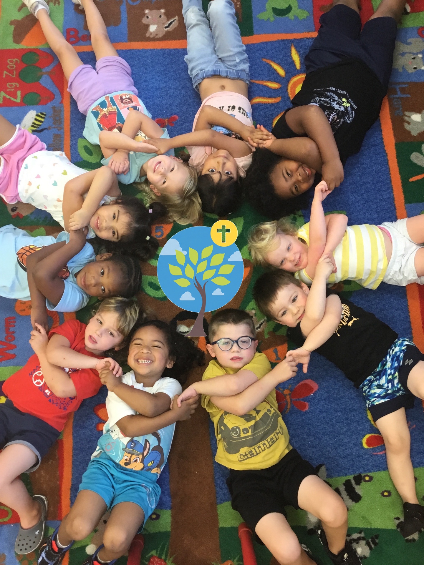 Children lying in a circle with the Bethany Early Learning Ministry tree logo at the center